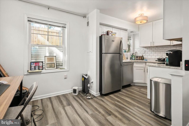 kitchen with backsplash, light stone counters, white cabinetry, stainless steel appliances, and hardwood / wood-style flooring