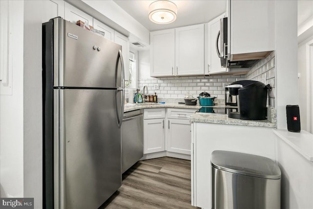 kitchen with light hardwood / wood-style floors, appliances with stainless steel finishes, white cabinetry, and decorative backsplash