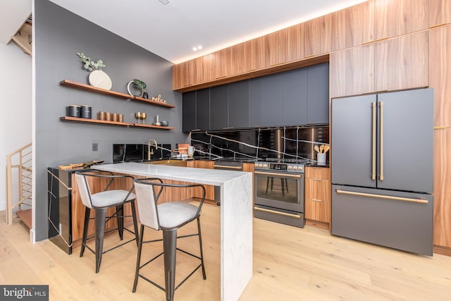 217 Tasker St, Philadelphia, PA 19148 - kitchen featuring stainless steel appliances, light wood-style flooring, decorative backsplash, a peninsula, and a kitchen bar