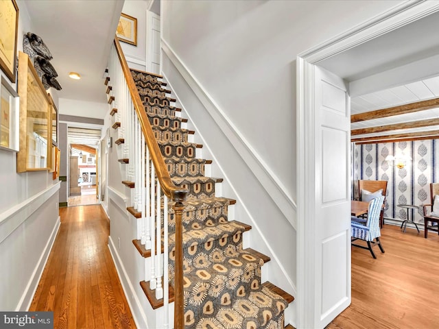 stairs featuring beam ceiling and wood finished floors