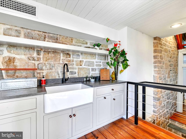 kitchen with visible vents, light wood finished floors, open shelves, a sink, and dark countertops