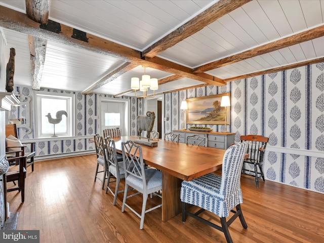 dining room featuring a notable chandelier, beamed ceiling, wallpapered walls, and hardwood / wood-style flooring