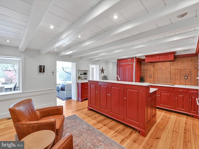 kitchen with beamed ceiling, light countertops, an island with sink, and light wood-style floors