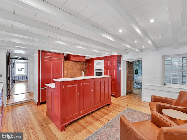 kitchen with a kitchen island with sink, light countertops, light wood-style floors, beamed ceiling, and reddish brown cabinets