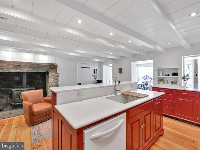 kitchen featuring beamed ceiling, light wood-type flooring, a center island with sink, a sink, and white dishwasher