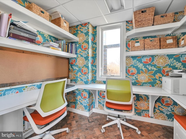 office space with brick floor, a drop ceiling, baseboards, and wallpapered walls