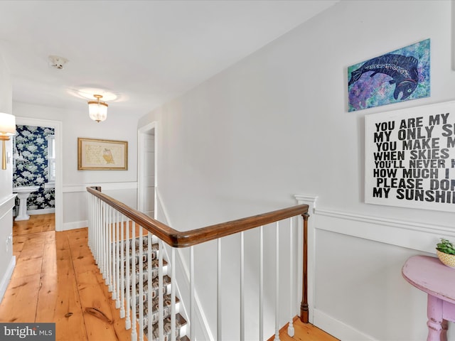 hallway with light wood-type flooring, an upstairs landing, and a wainscoted wall