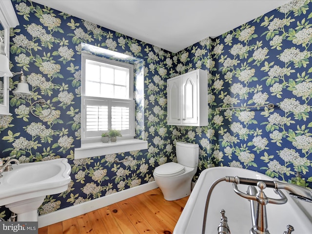 bathroom with baseboards, toilet, wood finished floors, and wallpapered walls