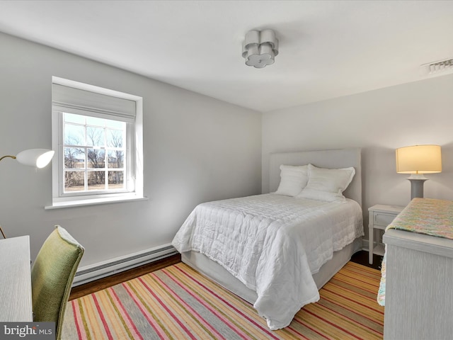 bedroom featuring a baseboard heating unit, wood finished floors, and visible vents