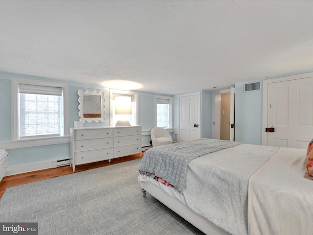 bedroom with a baseboard radiator, visible vents, wood finished floors, and a baseboard heating unit