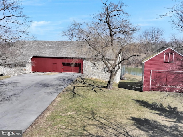 view of barn with aphalt driveway, a water view, and a yard