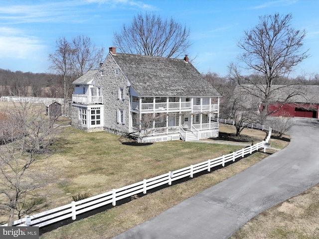 exterior space featuring a fenced front yard, a porch, a front yard, a chimney, and a balcony