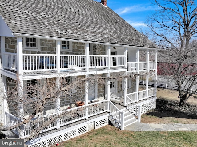 back of house with covered porch, stone siding, and a chimney