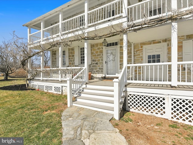 doorway to property with a yard, stone siding, covered porch, and a balcony