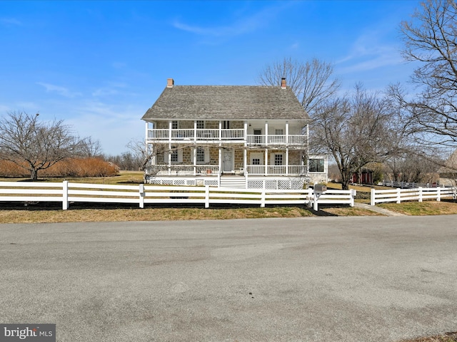 view of front of home with a balcony, covered porch, a fenced front yard, and a chimney