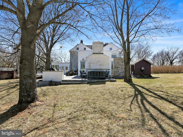 back of house with a yard, an outdoor structure, a chimney, and a shed