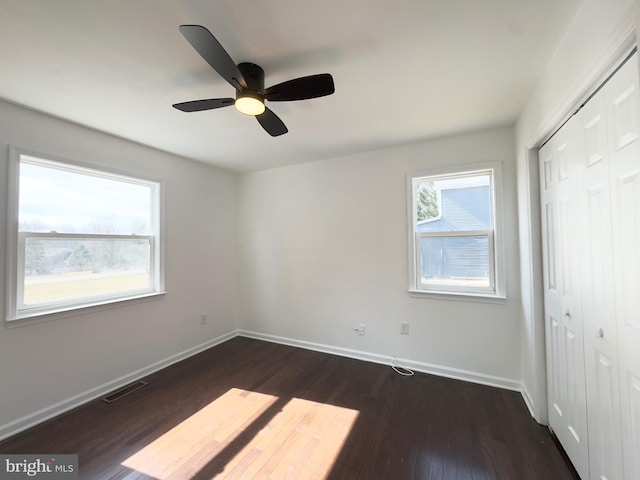 unfurnished bedroom featuring dark wood-type flooring, a closet, visible vents, and baseboards