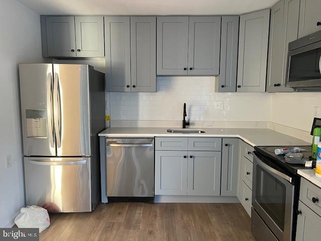 kitchen with dark wood-style floors, stainless steel appliances, light countertops, gray cabinetry, and a sink