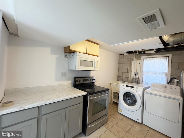 kitchen featuring electric stove, washing machine and clothes dryer, light countertops, visible vents, and white microwave