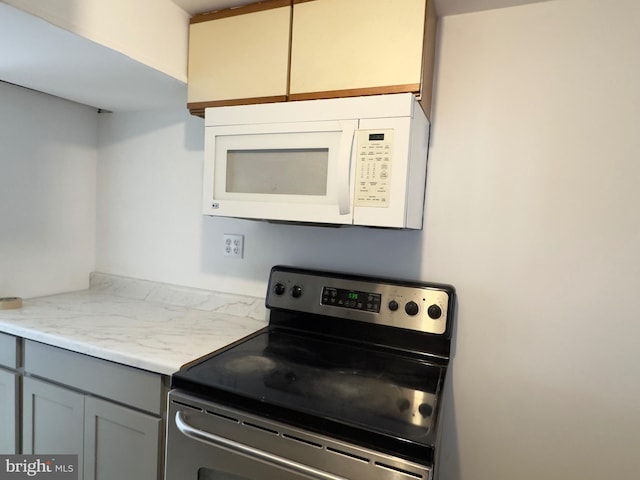 kitchen featuring light stone counters, gray cabinets, white microwave, and stainless steel electric stove