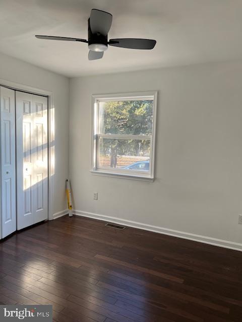 empty room with dark wood-type flooring, visible vents, ceiling fan, and baseboards