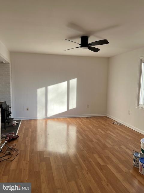 unfurnished living room featuring a wood stove, ceiling fan, baseboards, and wood finished floors