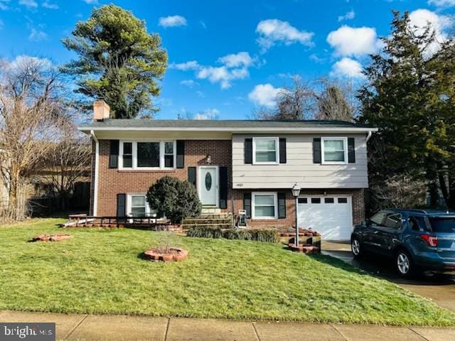 bi-level home featuring an attached garage, brick siding, driveway, a chimney, and a front yard