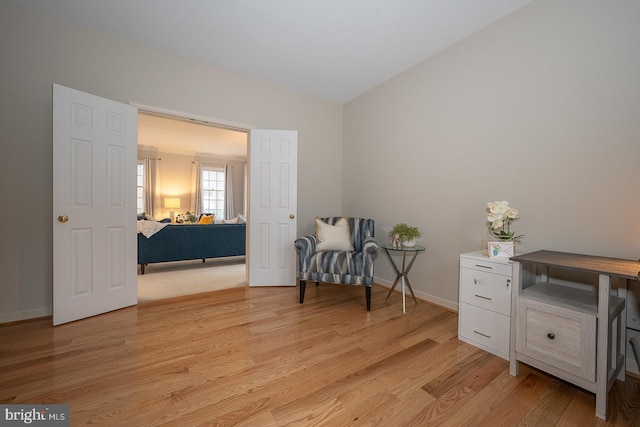 living area featuring lofted ceiling, baseboards, and light wood-style floors