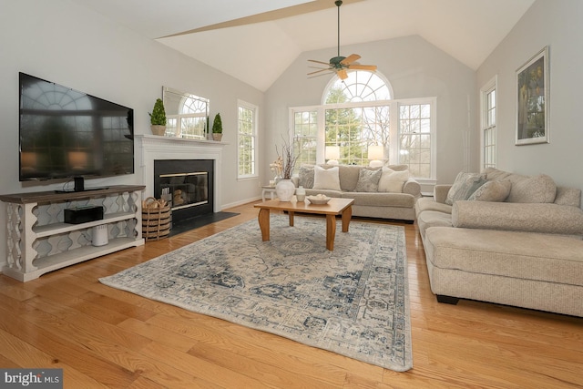 living area with a fireplace with flush hearth, high vaulted ceiling, wood finished floors, and a ceiling fan