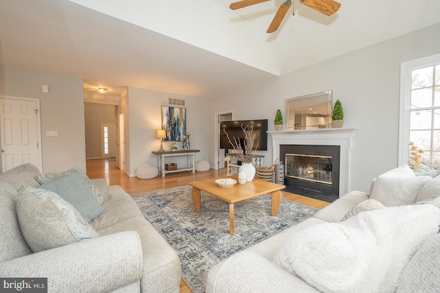 living area with lofted ceiling, visible vents, a fireplace with flush hearth, ceiling fan, and wood finished floors