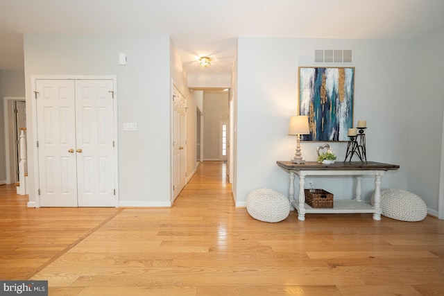 hall with light wood-style flooring, visible vents, and baseboards