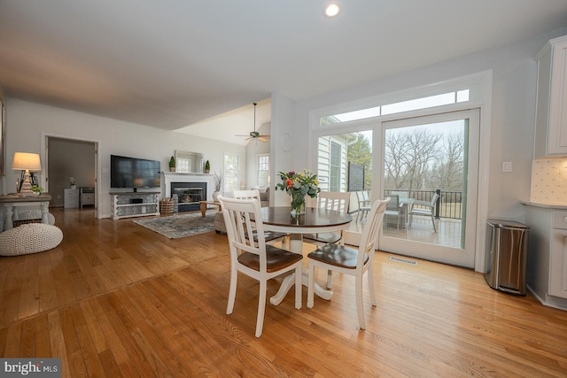 dining area featuring light wood finished floors, visible vents, a ceiling fan, and a glass covered fireplace