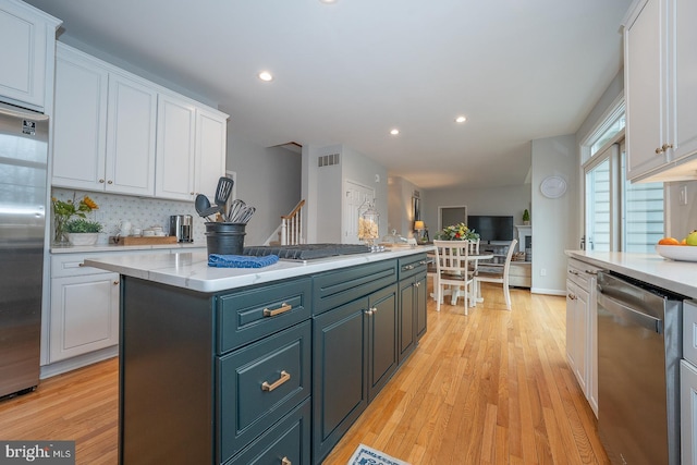 kitchen with tasteful backsplash, white cabinets, a kitchen island, appliances with stainless steel finishes, and light wood-type flooring