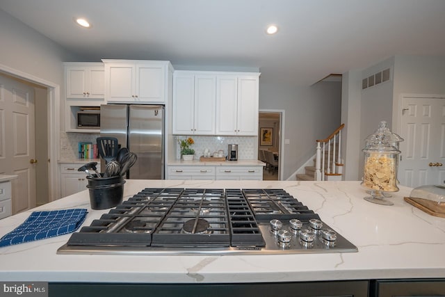 kitchen with appliances with stainless steel finishes, light stone countertops, visible vents, and white cabinetry