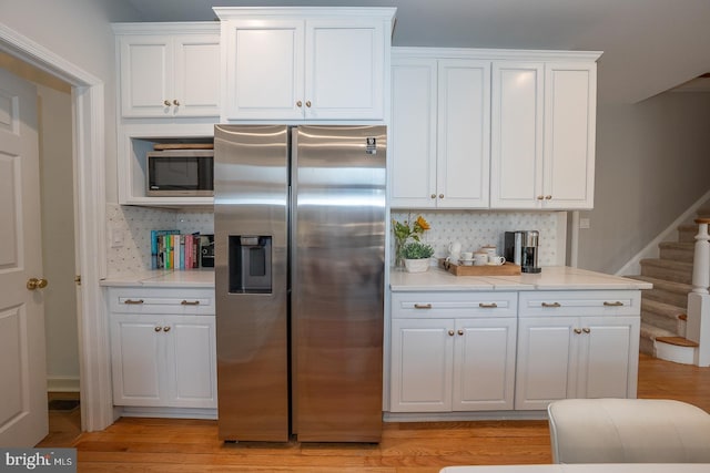 kitchen featuring stainless steel appliances, white cabinets, light wood-style flooring, and tasteful backsplash