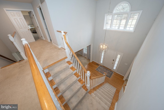 staircase with a high ceiling, wood finished floors, visible vents, baseboards, and an inviting chandelier