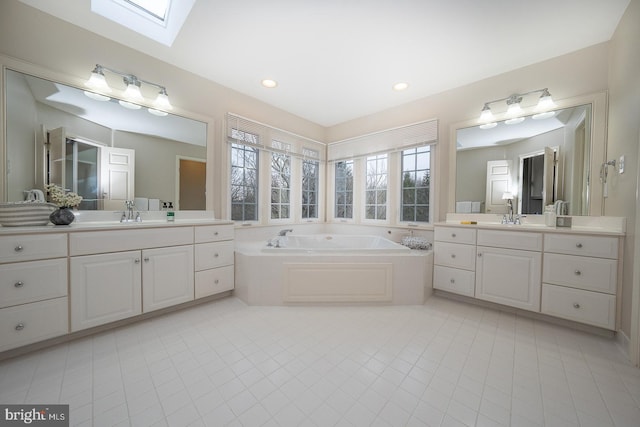 bathroom featuring a sink, a skylight, a garden tub, and two vanities