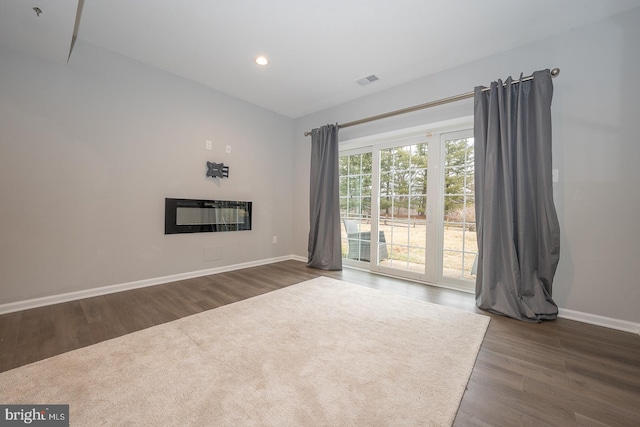 unfurnished living room with baseboards, visible vents, dark wood-type flooring, and a glass covered fireplace