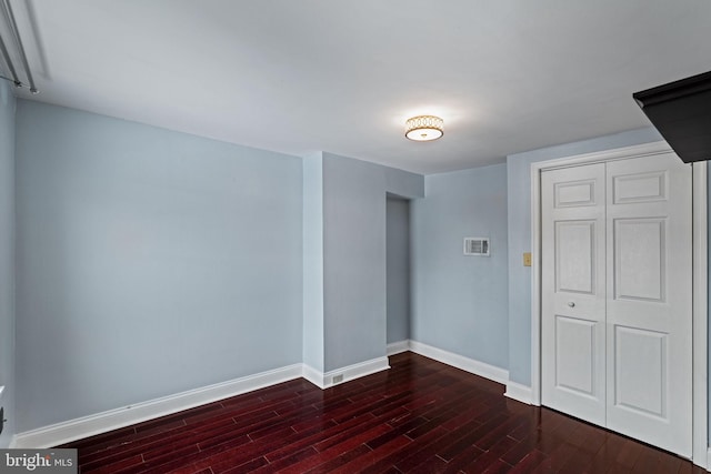 spare room with dark wood-style flooring, visible vents, and baseboards