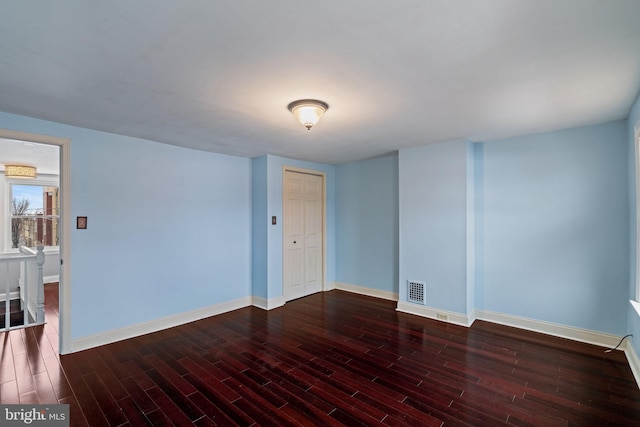 spare room featuring dark wood-style flooring, visible vents, and baseboards