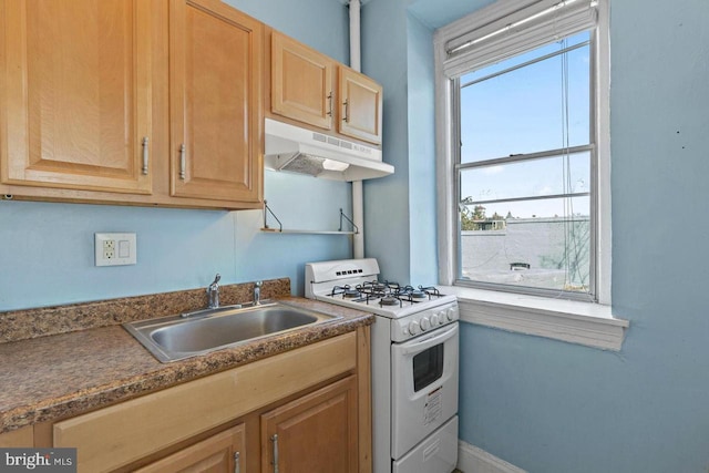 kitchen with white gas stove, dark countertops, a sink, under cabinet range hood, and baseboards