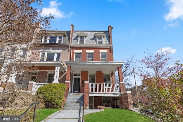 view of front of home with a porch, a front yard, brick siding, and mansard roof