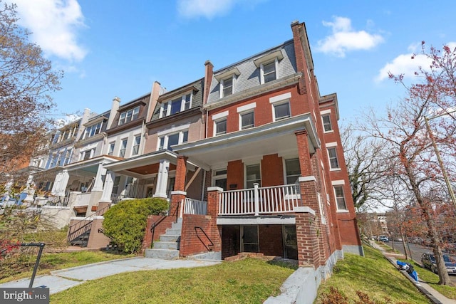 townhome / multi-family property featuring brick siding, mansard roof, covered porch, a high end roof, and a front lawn