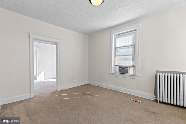 spare room featuring a textured ceiling, cooling unit, light colored carpet, baseboards, and radiator heating unit