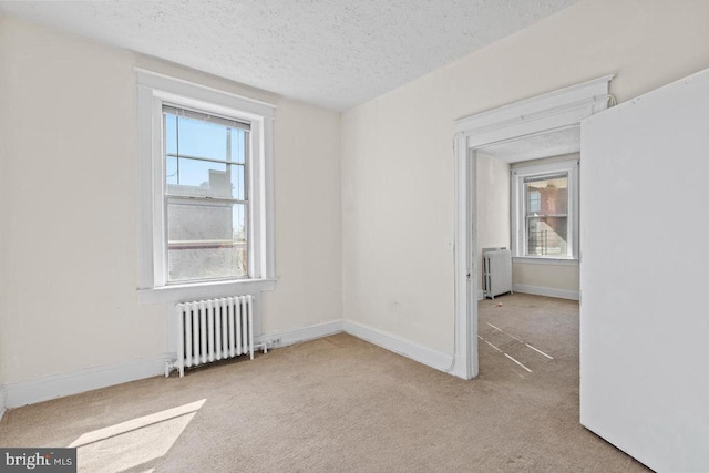 spare room featuring radiator, light carpet, baseboards, and a textured ceiling