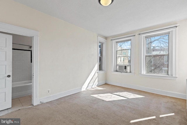 spare room with a textured ceiling, light tile patterned flooring, cooling unit, light carpet, and baseboards