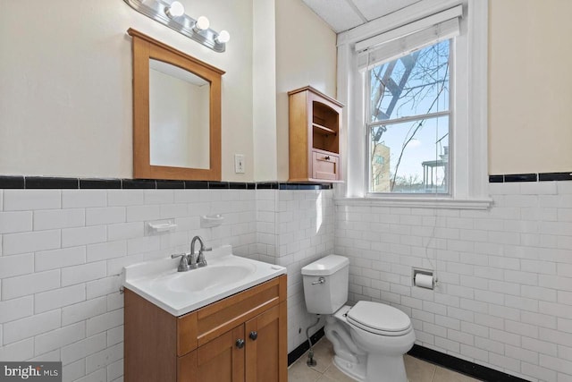 bathroom featuring toilet, a wainscoted wall, tile patterned flooring, vanity, and tile walls