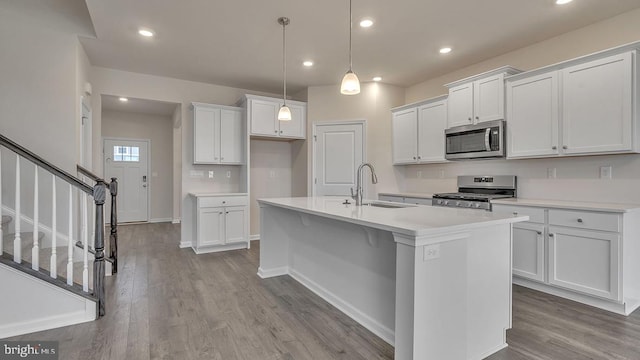 kitchen with appliances with stainless steel finishes, hanging light fixtures, sink, white cabinetry, and a kitchen island with sink