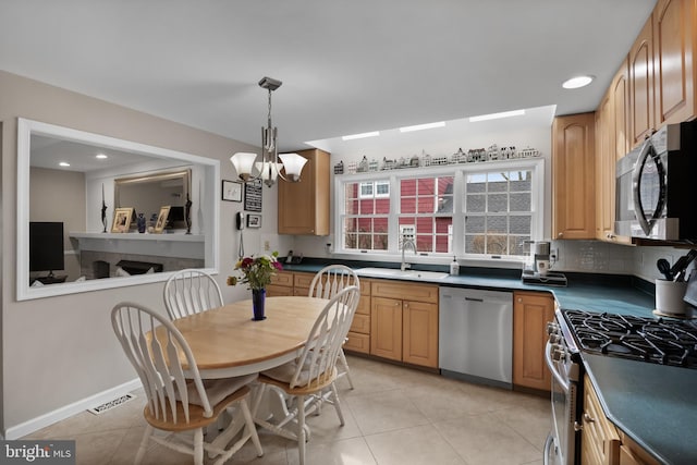 kitchen with light tile patterned floors, stainless steel appliances, a sink, hanging light fixtures, and dark countertops