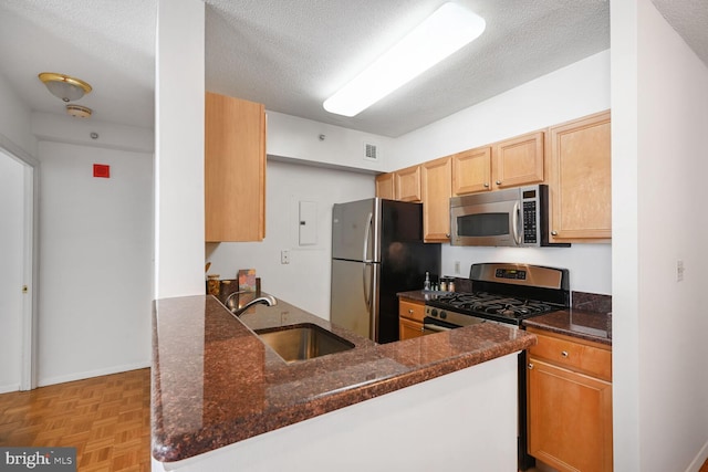 kitchen with a textured ceiling, dark stone counters, stainless steel appliances, and a sink